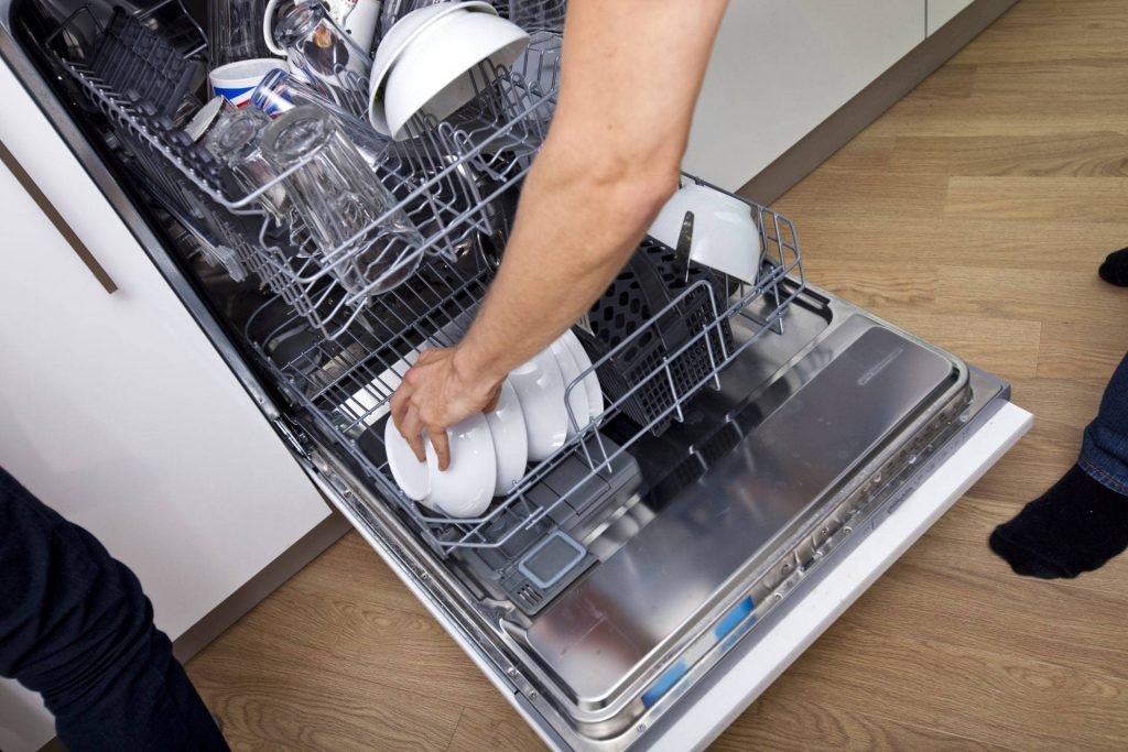 A man carefully places dishes into a dishwasher, preparing for a thorough clean in the kitchen.